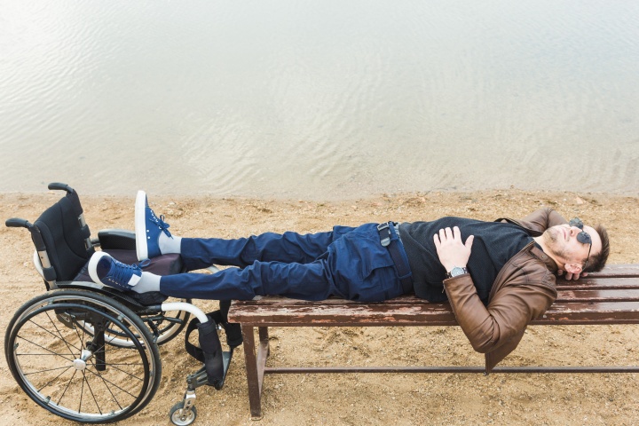 man lying on a bench with feet on a wheelchair